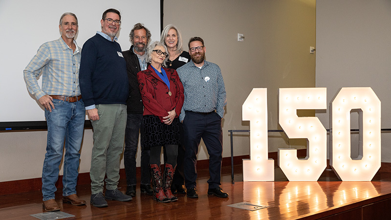 Michael Branch stands with five others at the 2023 Nevada Writers Hall of Fame event beside a large, lit up 150 sign.