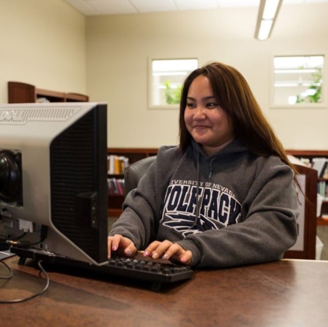 Student wearing a Wolf Pack sweatshirt typing on a computer at the Knowledge Center