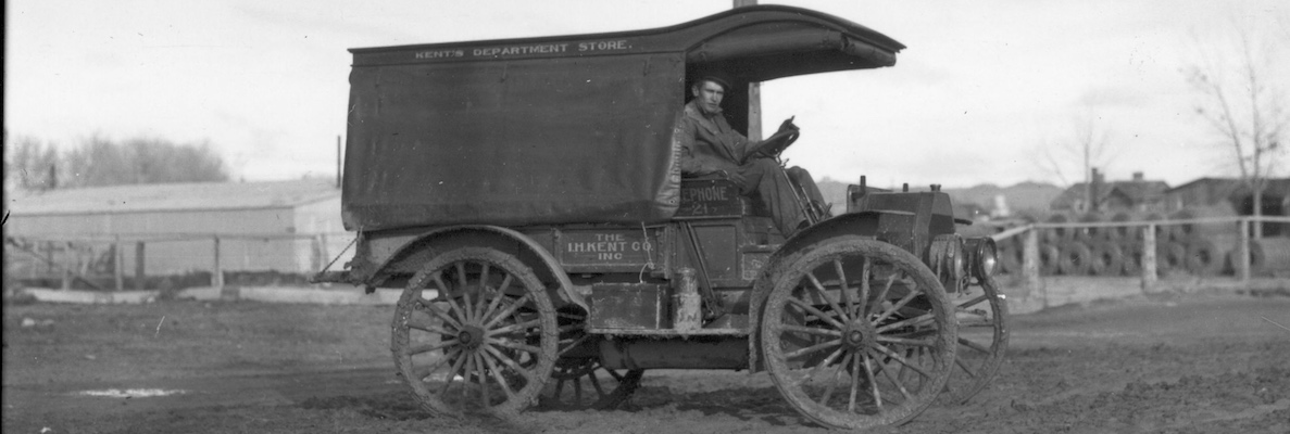 A delivery truck and driver from The I. M. Kent Company, Kent's Department Store. The driver looks out over a muddy road with a disinterested look at the camera.