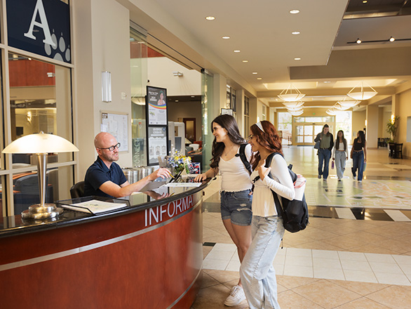 Two visitors speak with a staff member at an information desk in the Knowledge Center lobby.