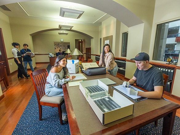 People examine archival materials at tables in a library research room.