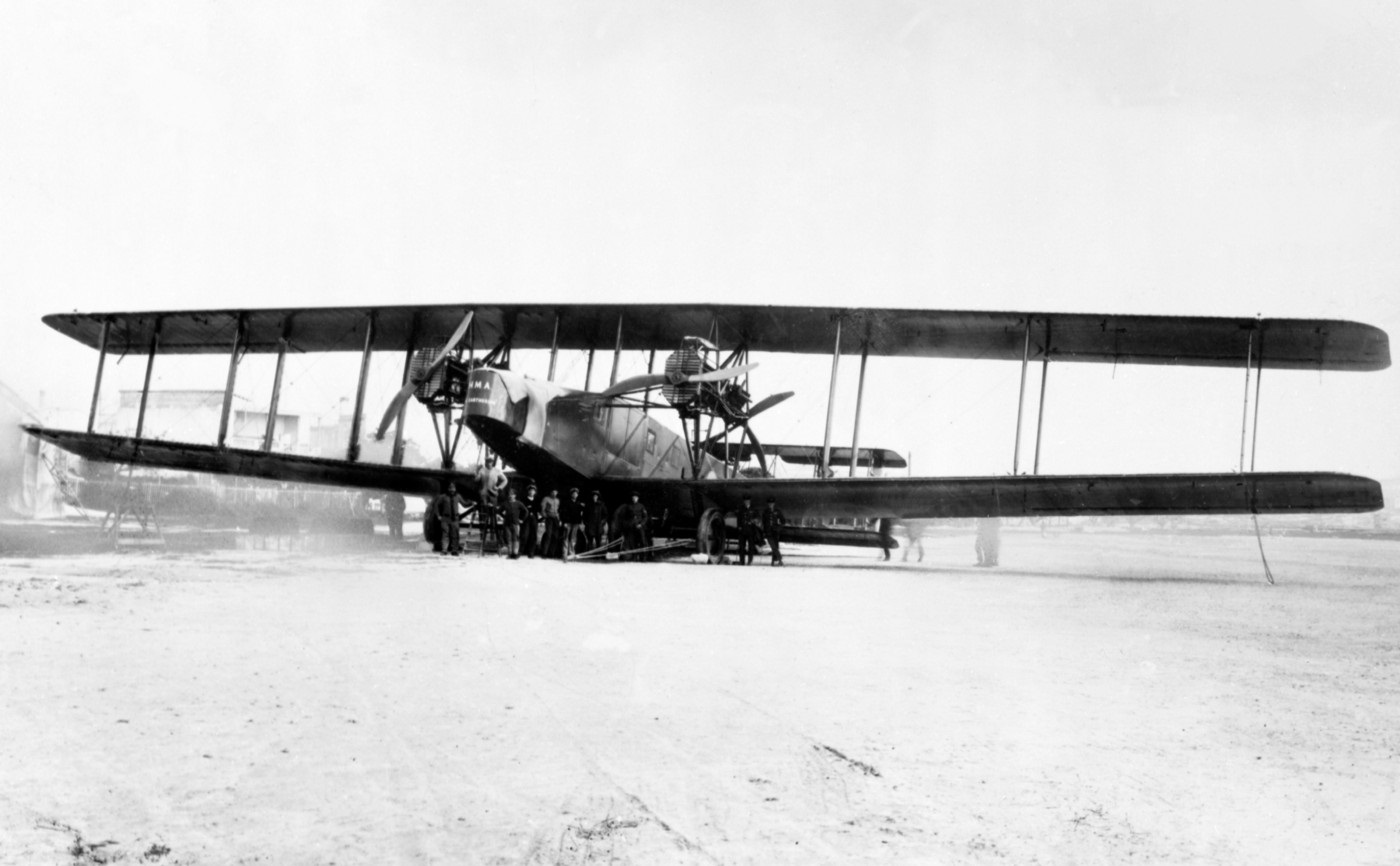 Black and white photograph of a biplane with people standing in front