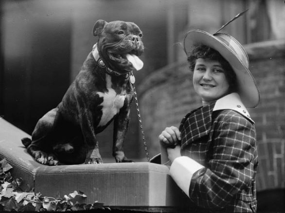 A black and white image of a woman in a hat next to a french bulldog