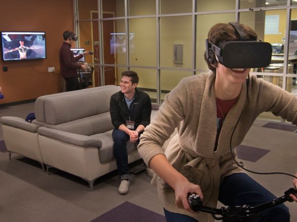 Students using AtReality including one looking at a monitor, one sitting on a couch, and one riding a stationary bike while wearing a VR headset