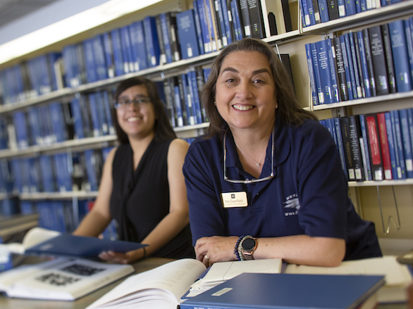 Team members standing in front of blue thesis volumes in the DeLaMare library.