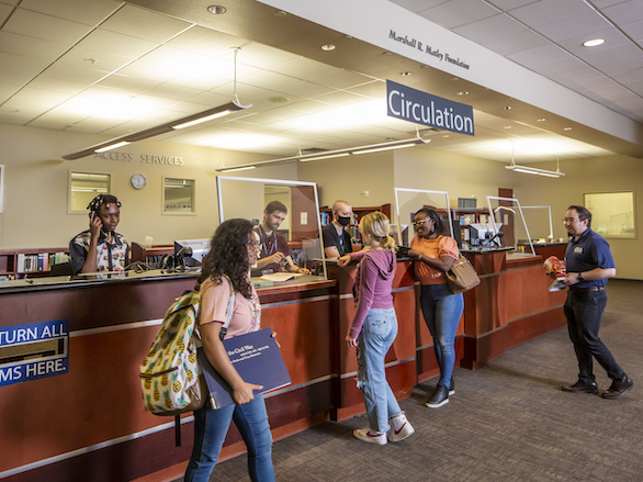 Patrons working with team members at the circulation desk to check out or renew materials.