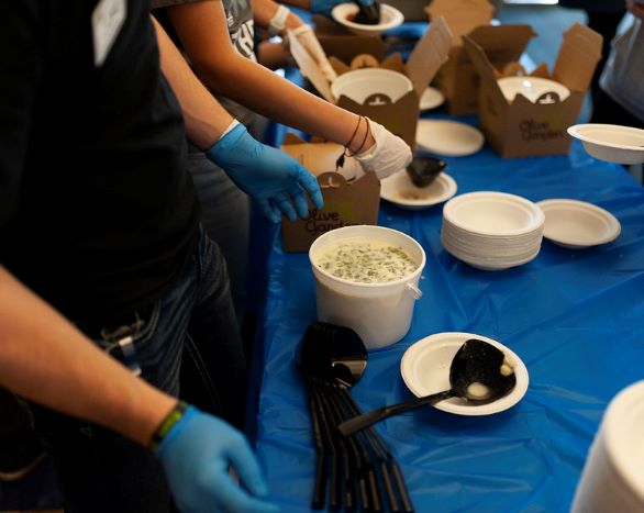 Students serving hot meals in paper cups and plates in the KC breezeway