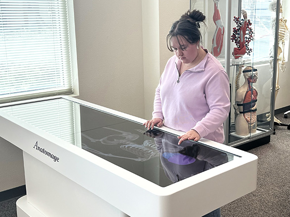 A woman stands by the Anatomage table which shows a digital skeleton.