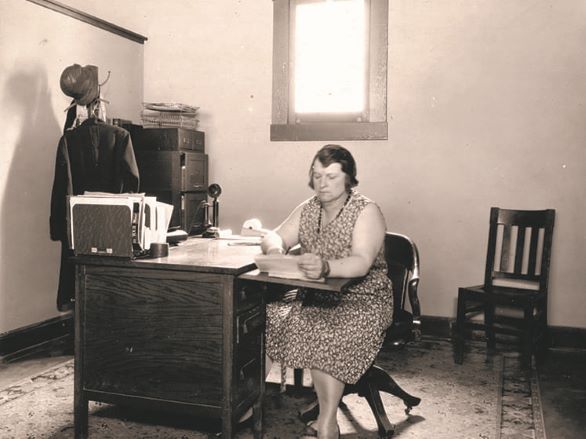 Black and white photograph of a woman in a house dress typing at a typewriter