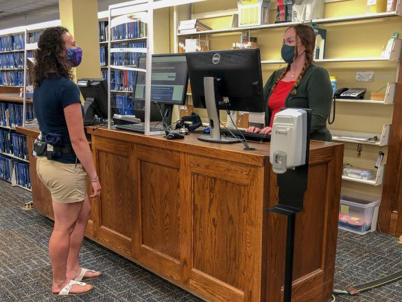 A student and a worker at a service desk at DeLaMare wearing masks with a protective barrier