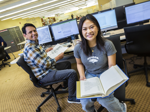 Team member at DeLaMare Library working with a student in front of a set of computers.