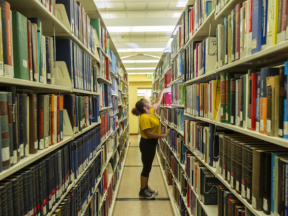 Student browsing materials in the stacks of DeLaMare Library.