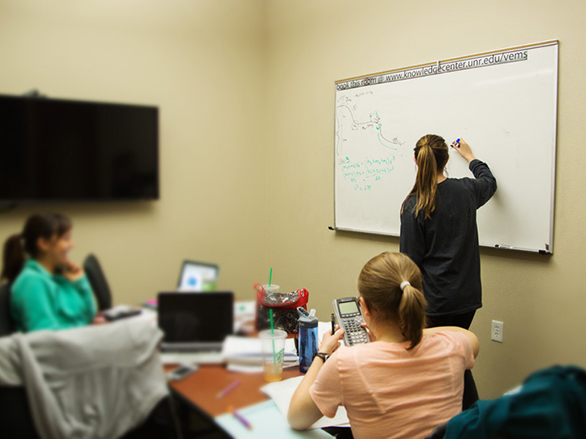 Students sitting at desks and writing on a white board in a group study room