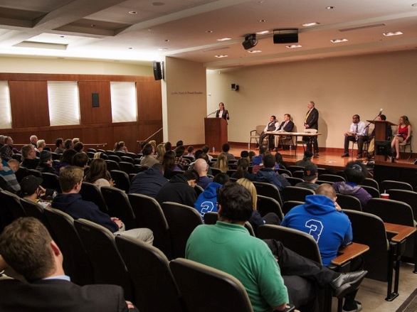 People seated at an event in the Wells-Fargo Auditorium with several people on stage