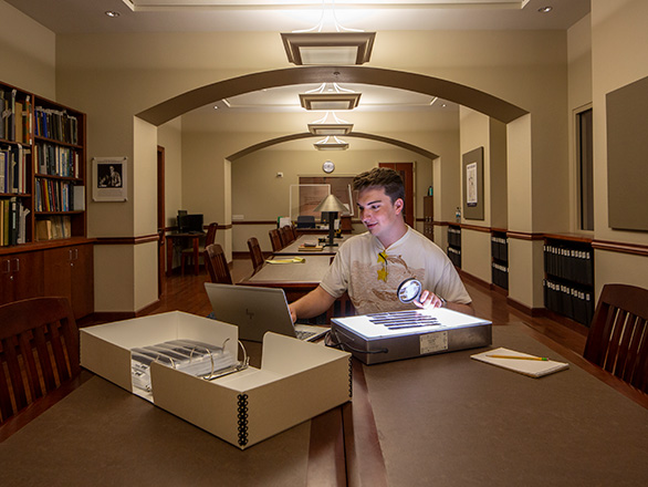 A student works in the SCUA reading room and holds a magnifying glass by a light box.