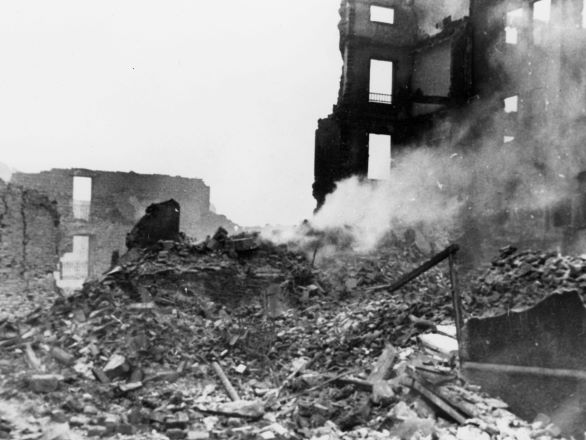 Burning and blackened ruined buildings with rubble in the foreground