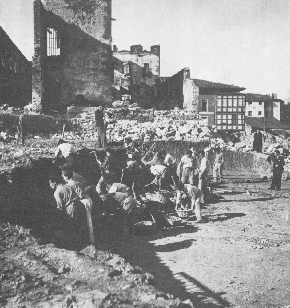Black and white photograph of POWs in front of a ruined building in Gernika