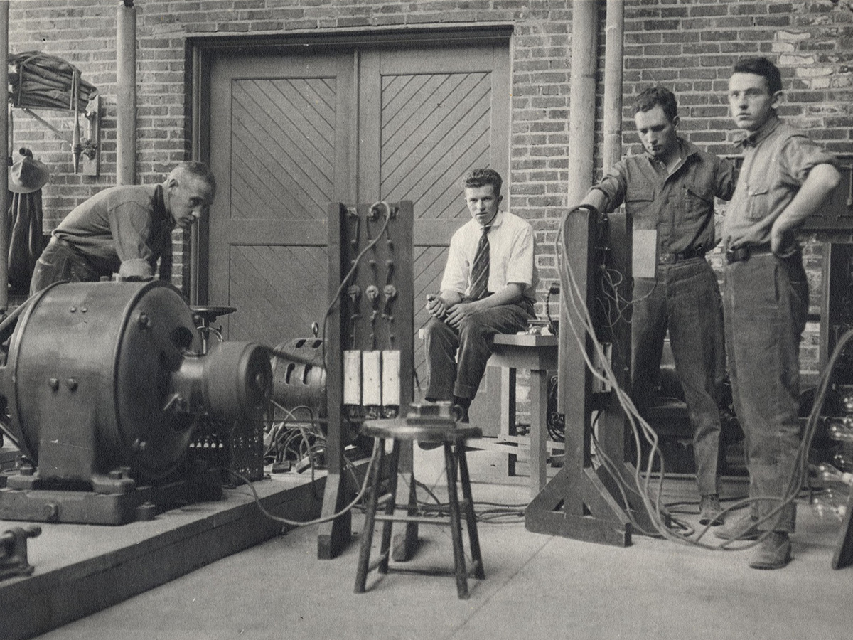 Students stand around an electrical machine and a generator.