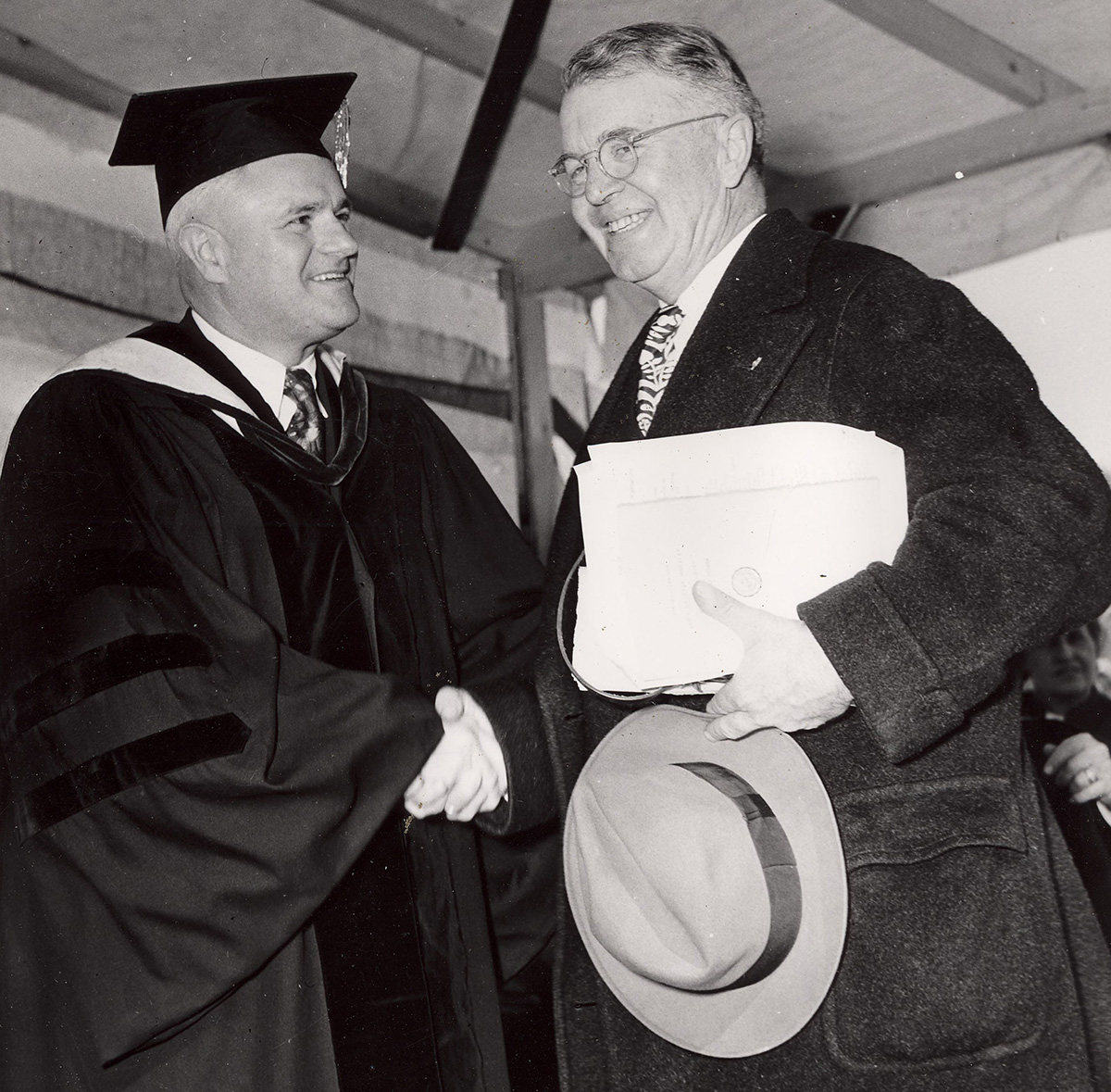 John O. Moseley, left, shakes hands with a man in academic attire.