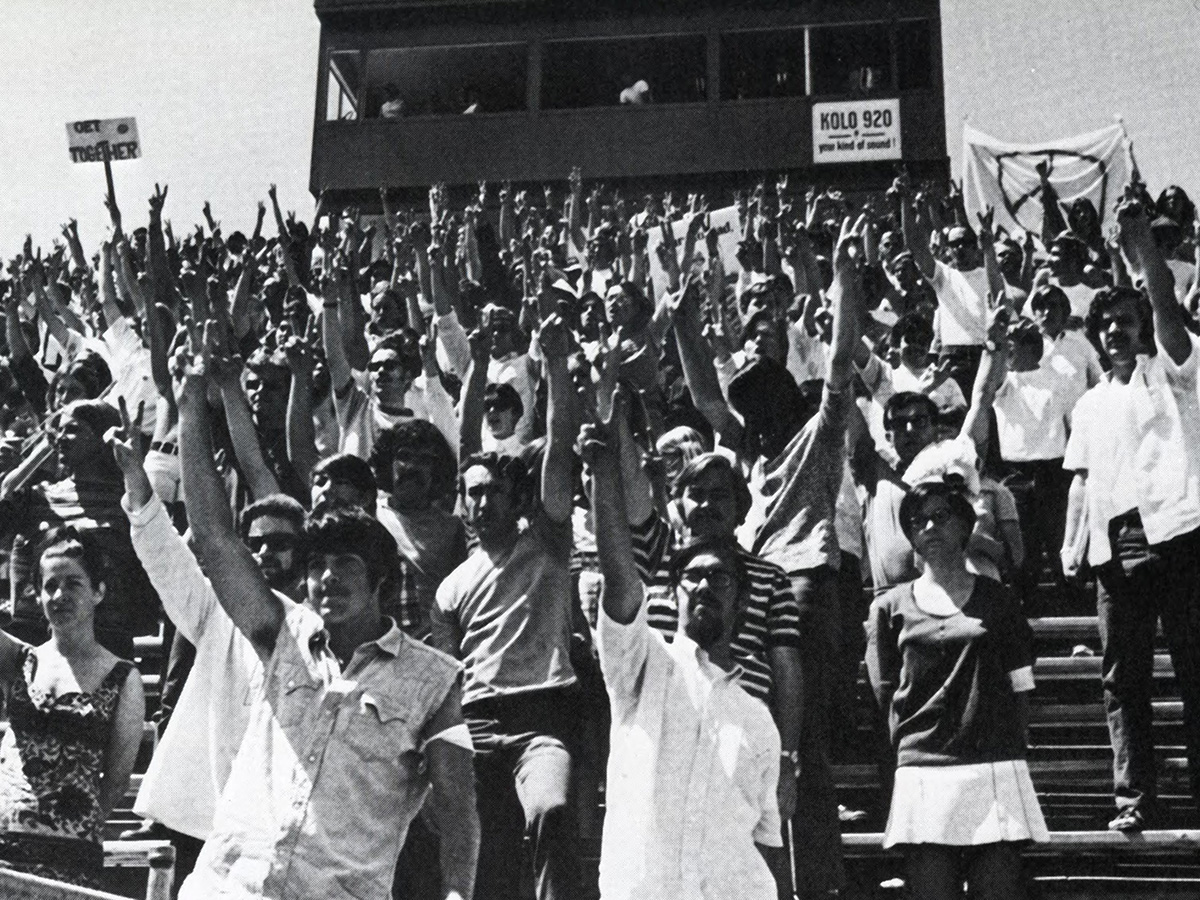 Protestors stand in the bleachers and press box showing peace signs with their fingers during an ROTC awards ceremony in Mackay Stadium during a student-led Vietnam War Protest on Governor's Day.