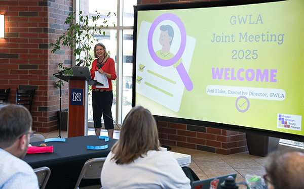 GWLA director Joni Blake stands at a podium at the front of a room. The screen behind her reads: "GWLA Joint Meeting 2025 Welcome Joni Blake, Executive Director, GWLA"