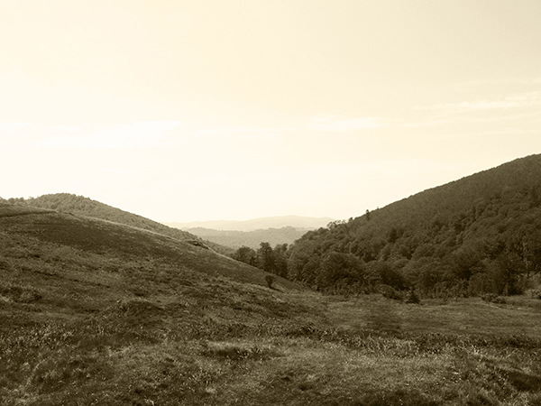 A sepia toned view of a field surrounded by hills.