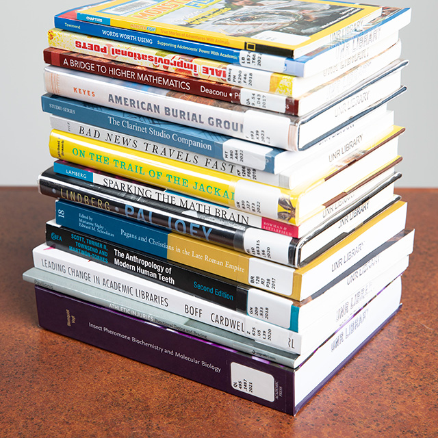 A stack of books written by faculty authors sits on a table.