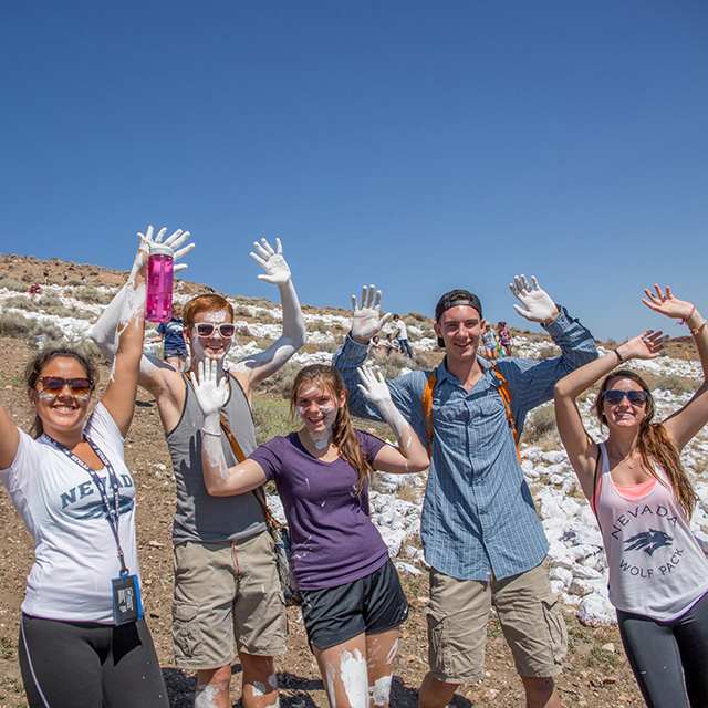 Students pose with painted hands in the air in front of the painted "N" on Peavine Peak.